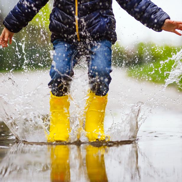 Close up legs of child with yellow rubber boots jump in puddle on an autumn walk