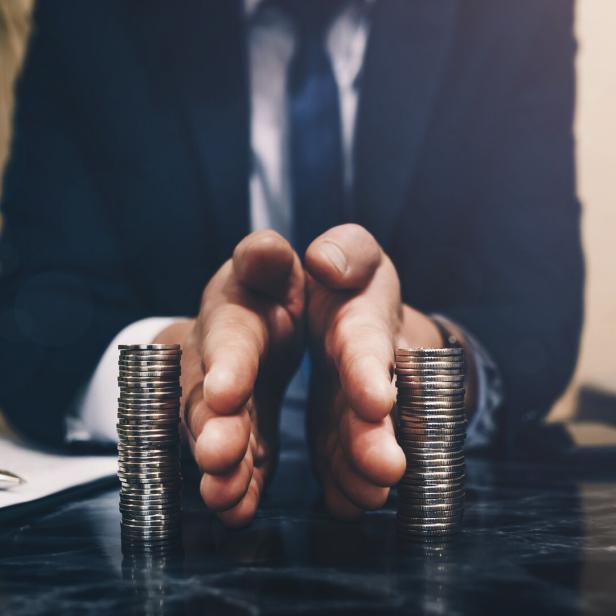 Ein Mann im Anzug trennt mit den Händen zwei Stapel Münzen auf einem Tisch voneinander.