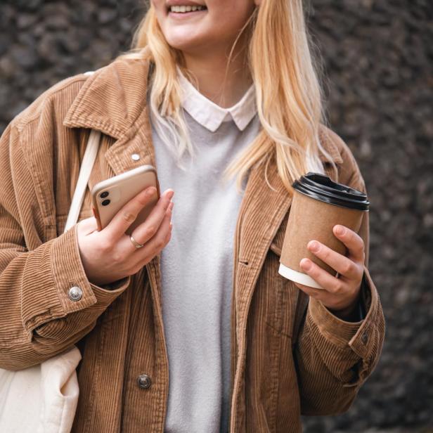 Nahaufnahme, eine Tasse Kaffee und ein Smartphone in weiblichen Händen in der Stadt