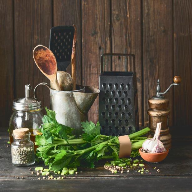 Rustic cooking set with vintage kitchen utensils and celery bunch on dark table at wooden background. - Stock-Fotografie
