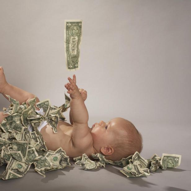 Baby girl (5 months) lying down covered with us dollar bills falling from above - Stock-Fotografie