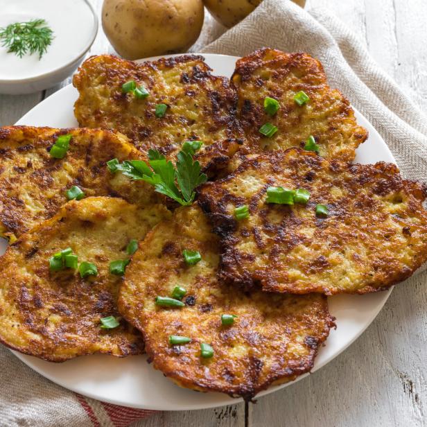 Ein Teller Kartoffelpuffer, garniert mit Schnittlauch und Petersilie, dazu ein Schälchen Sour Cream.
