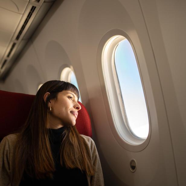 Junge Frau, die mit dem Flugzeug reist und aus dem Fenster schaut - Stock-Fotografie