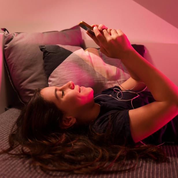 Symbolbild: Eine Frau liegt auf dem Bett und benutzt ihr Smartphone.