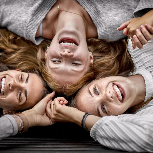 Three happy young women lying on a bench holding hands - Stock-Fotografie