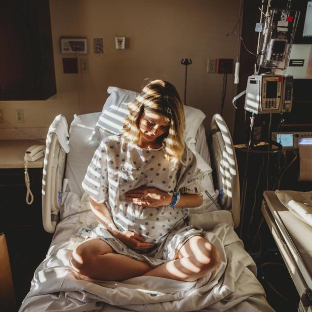 Pregnant woman touching stomach while sitting on bed in hospital - Stock-Fotografie