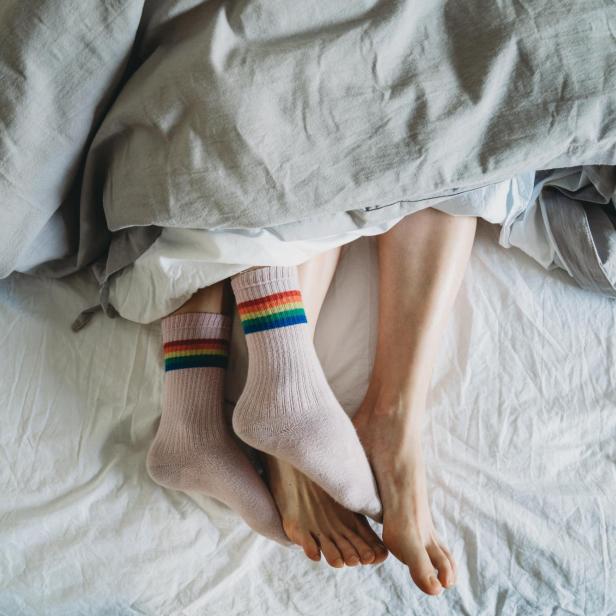 zwei Menschen liegen im Bett, eine Person trägt Socken, die andere nicht