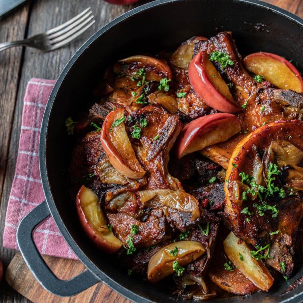 Braised pork cutlets with apples and onions in a roasting pot on wooden table