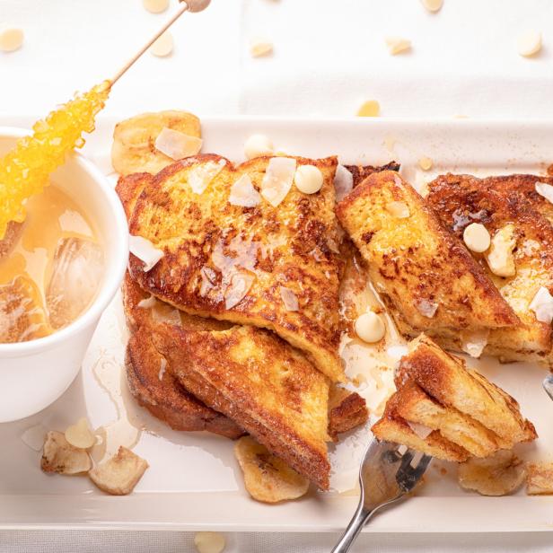 Top view french toast sliced and fried with honey, maple syrup and butter. Served on a white plate with silverware and cup of coffee.