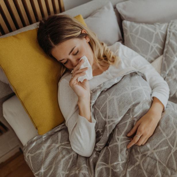 Eine Frau liegt im Bett und schnäuzt sich.