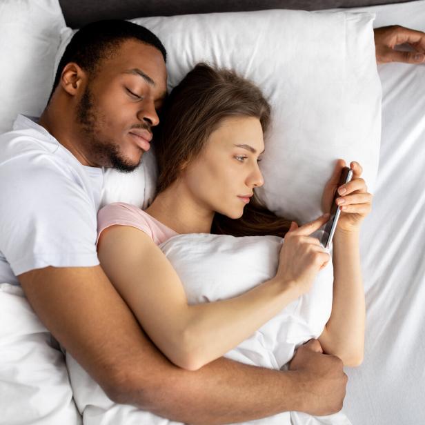 Mann und Frau liegen im Bett, Frau ist am Handy