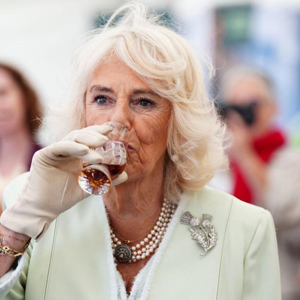 Queen Camilla trink aus einem kleinen Glas.