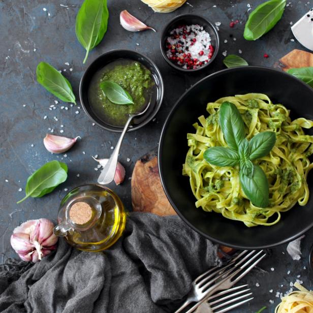 Pasta tagliatelle with pesto sauce and fresh basil leaves in black bowl.