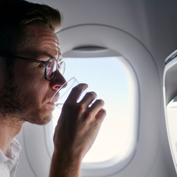 Mann sitzt im Flugzeug und trinkt Wasser