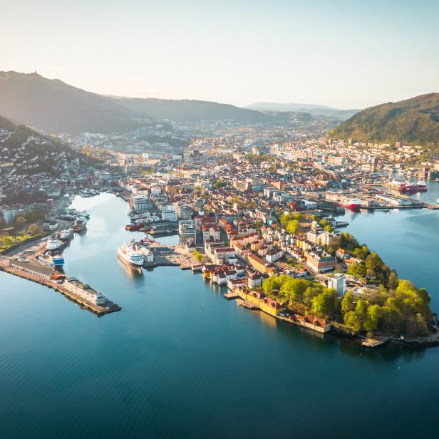 Blick auf Bergen mit der Bucht Vågen und dem historischen Stadtkern (links), den namensgebenden Hügeln und dem Hafen, an dem die bekannte Kreuzfahrtroute Hurtigruten beginnt (rechts)