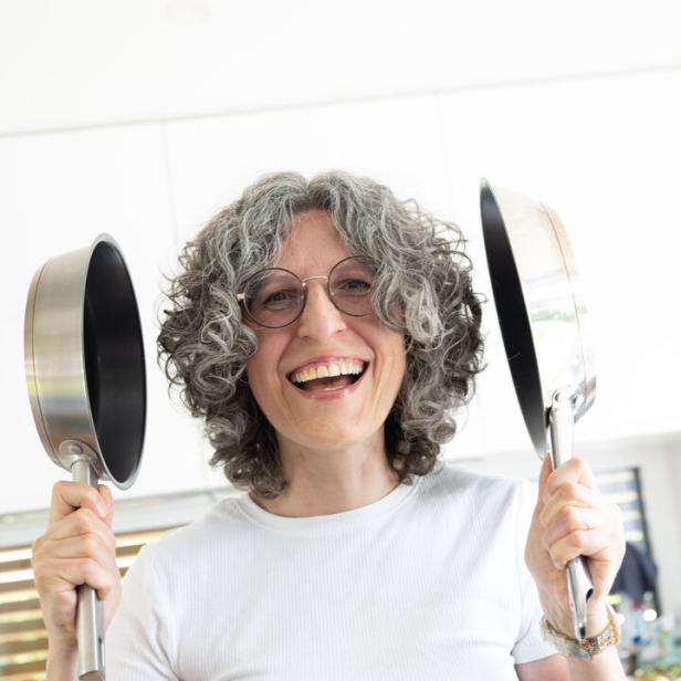 Elisabeth Koller hält lachend zwei Bratpfannen in die Höhe.