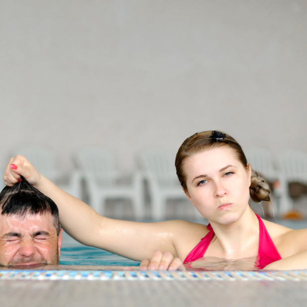 Frau und Mann im Pool, sie ist böse auf ihn und taucht ihn unter. Streit im Urlaub