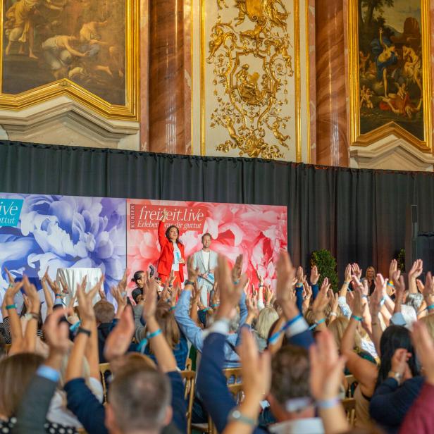 Ein barocker Festsaal mit vielen Besuchern, die die Hände in die Höhe reißen