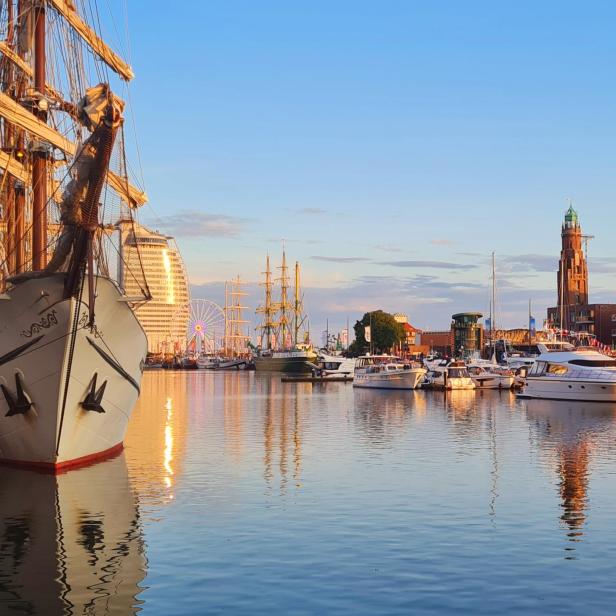 Ein Hafen voller Schiffe mit einem Riesenrad im Hintergrund im Sonnenuntergang.