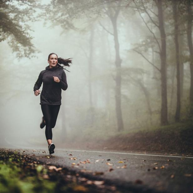 Junge Frau läuft im Wald bei nebligem Wetter. 