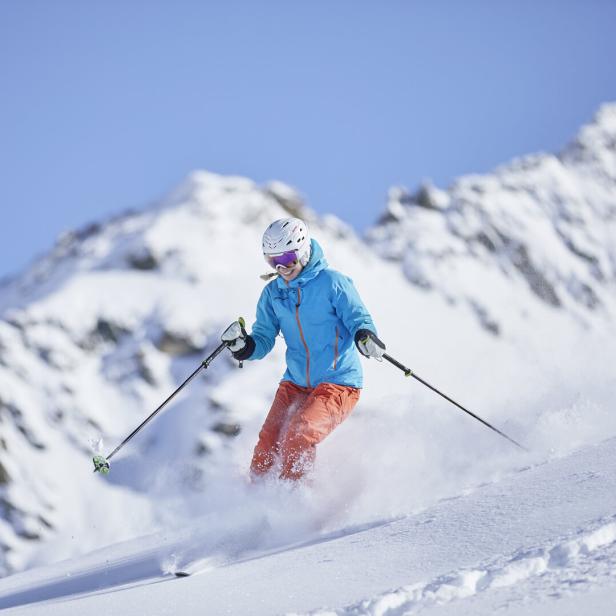 Skifahrerin wedelt über die Piste, der Schnee staubt