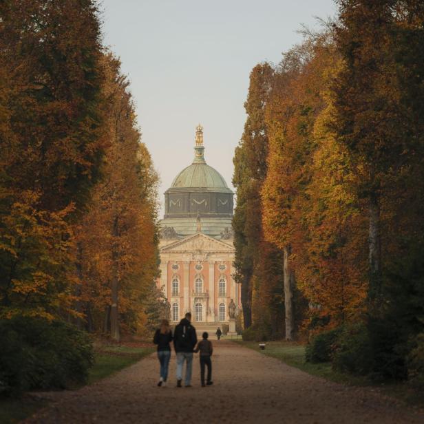 3. Ein Paar genießt einen Spaziergang mit ihrem Hund auf einem ruhigen Weg in der Natur. Am Ende des Weges steht ein Schloss.