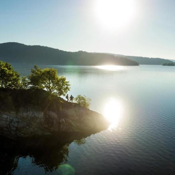 Zwei Personen stehen auf einem Felsen am Ufer eines Sees im Morgenlicht.