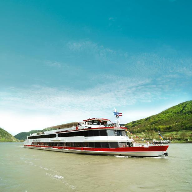 Die MS Admiral Tegelthoff auf der Donau. Im hintergrund sind Weinberge zu sehen. Der Himmel ist blau.