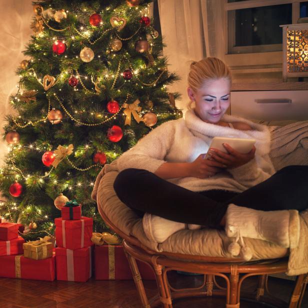 Frau sitzt vor dem Christbaum und liest ein Buch.