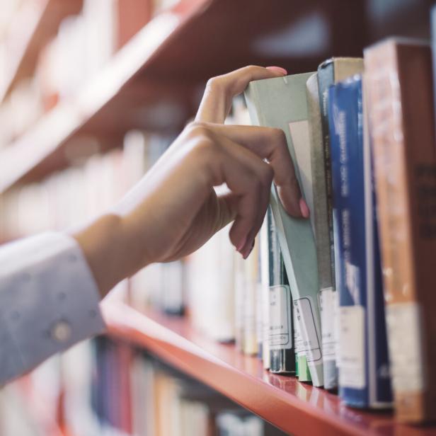 Frau nimmt sich ein Buch aus dem Regal.