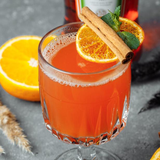 Ein Glas mit einem orangefarbenen Getränk, garniert mit Orange, Zimtstange und Minze.