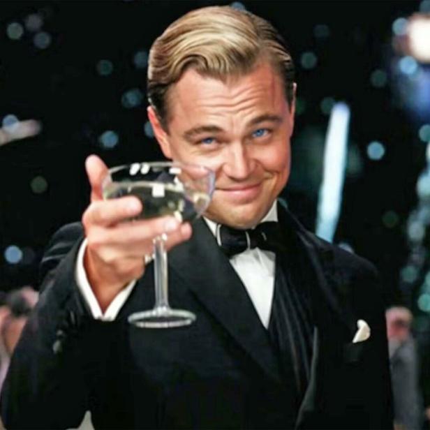 Der große Gatsby im Smoking, gespielt von Leonardo DiCaprio, prostet mit einer Champagnerschale. Im Hintergrund explodiert ein Feuerwerk.