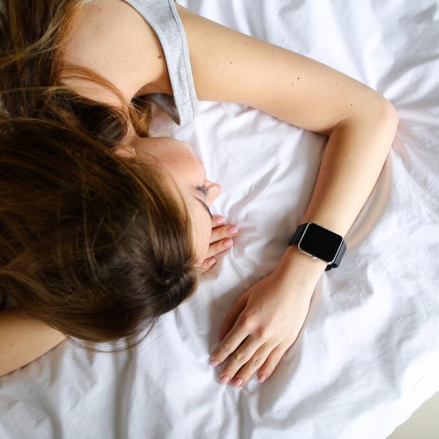 eine Frau liegt schlafend mit einer Smartwatch am Handgelenk im Bett