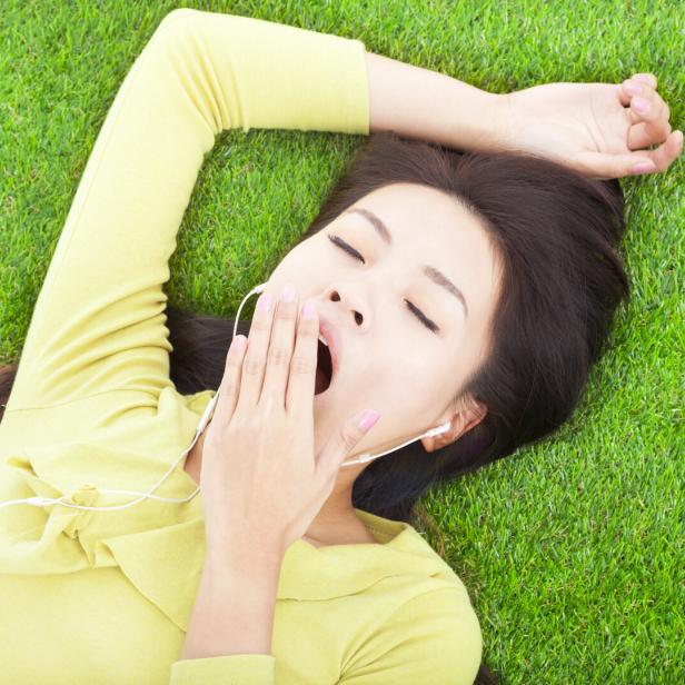 Eine Frau liegt im Gras und gähnt.