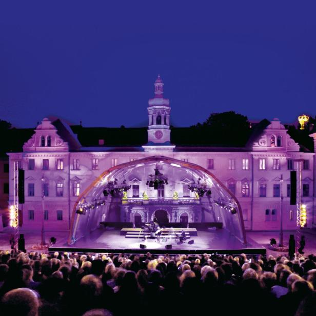 Eine Open-Air-Veranstaltung mit einer Bühne vor einem historischen Gebäude zieht viele Zuschauer an.