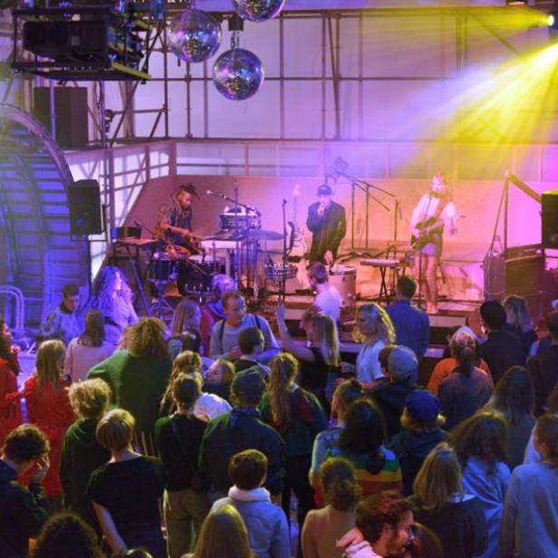 Eine Band spielt vor einem Publikum in einer Halle mit Discokugeln und Bühnenbeleuchtung.