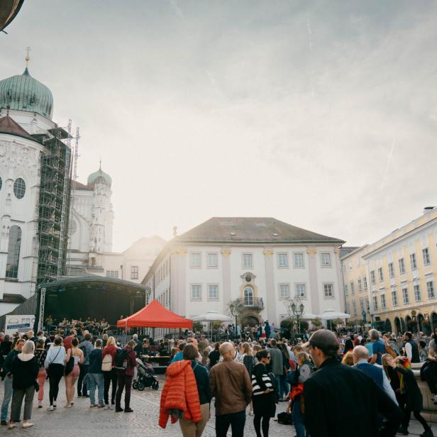 Eine Menschenmenge versammelt sich auf einem Platz vor einer Kirche und einem Brunnen.