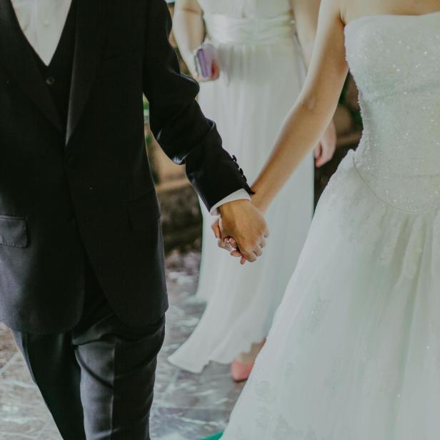 Frau im weißen Brautkleid Hand in Hand mit Mann im schwarzen Anzug.