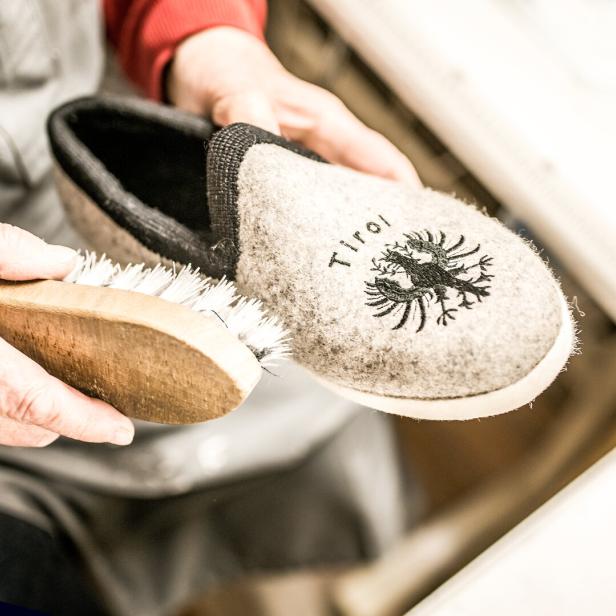 Eine Person bürstet einen grauen Filzpantoffel mit Tiroler Adler-Emblem.