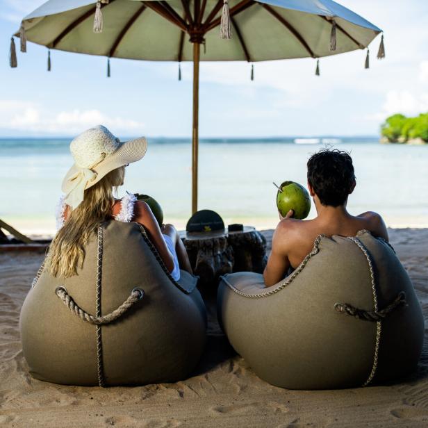 Rear view of a couple relaxing in bean bags on the beach.