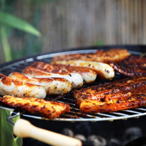 Auf einem Grill liegen Würstchen und mariniertes Fleisch.