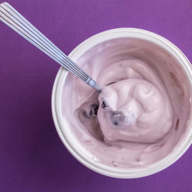 Joghurtbecher mit Heidelbeerjoghurt, Löffel und Deckel.