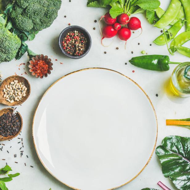Fresh greens, vegetables and grains with white plate in center Fresh greens, vegetables and grains with white plate in center