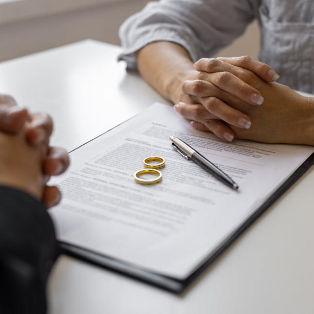Mein Partner will einen Ehevertrag. Ist das nötig? Partner sitzen gegenüber am Tisch liegt ein Vertrag