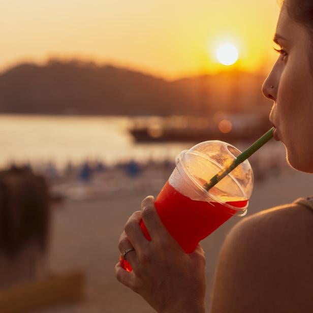 Eine junge Frau schlürft genüsslich einen Slushie im Sonnenuntergang an einem Seeufer
