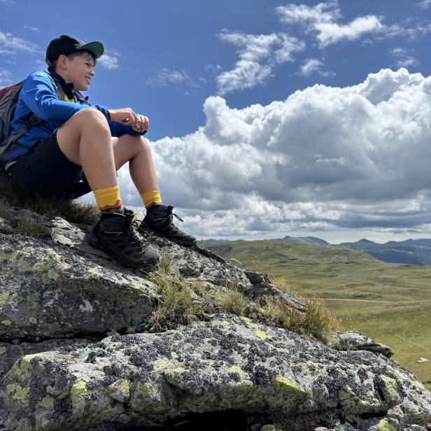 Kind sitzt auf einem Felsen und schaut in die Landschaft
