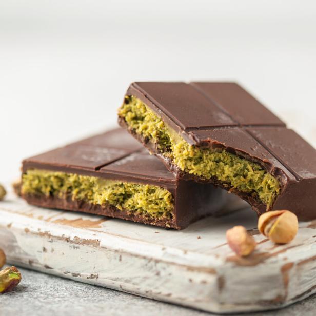 Zwei Stücke Dubai-Schokolade mit Pistazienfüllung auf einem Holzbrett.
