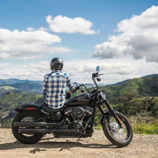 Ein Mann sitzt auf einem Motorrad vor einer bergigen Landschaft mit See vor ihm.