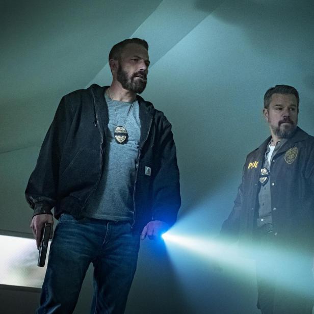 Matt Damon und Ben Affleck als Polizisten mit Dienstmarke, Taschenlampe und gezogener Waffe.