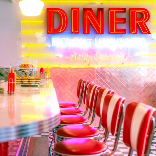 Das Interieur eines leeren Diners mit roten Barhockern und Neonreklame.